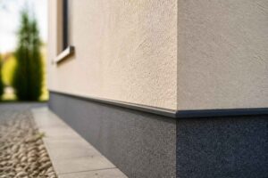 Zbliżenie narożnika domu z jasną elewacją i grafitowym cokołem przy ścieżce ogrodowej