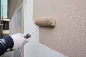 Dłoń w rękawiczce maluje zewnętrzną ścianę budynku wałkiem malarskim
