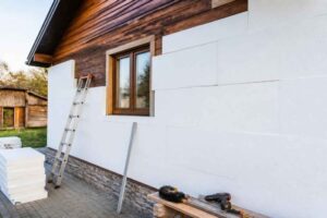 Biała elewacja domu podczas ocieplania, z drabiną, narzędziami i materiałami budowlanymi przed budynkiem