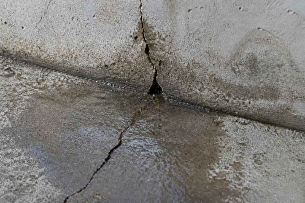 Pęknięcie betonowej posadzki przy łączeniu ze ścianą, z widoczną wilgocią i zabrudzeniami