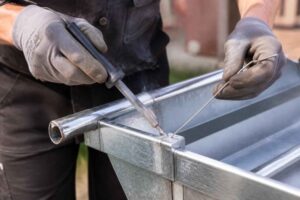 Pracownik w rękawicach spawa metalową konstrukcję z ocynkowanych profili stalowych