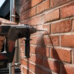 Pracownik wierci otwór w ceglanej ścianie za pomocą młotowiertarki akumulatorowej