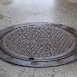 Okrągła żeliwna pokrywa włazu z napisem SEWER na betonowej nawierzchni