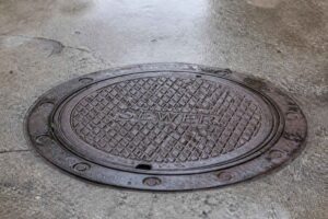 Okrągła żeliwna pokrywa włazu z napisem SEWER na betonowej nawierzchni
