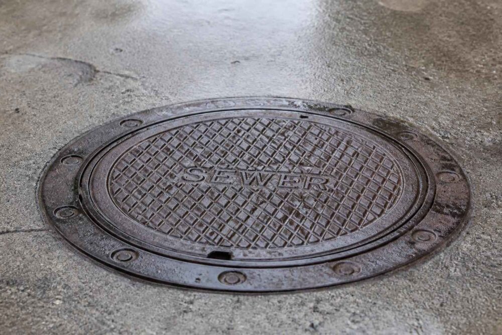 Okrągła żeliwna pokrywa włazu z napisem SEWER na betonowej nawierzchni
