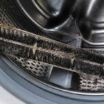 Zużyta, zabrudzona szczotka leżąca w bębnie pralki automatycznej