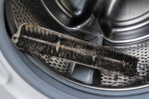 Zużyta, zabrudzona szczotka leżąca w bębnie pralki automatycznej